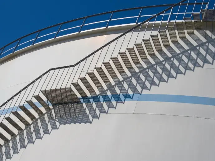 Industrial metal staircase against a white fuel storage tank under a clear sky / Huron Smith Oil